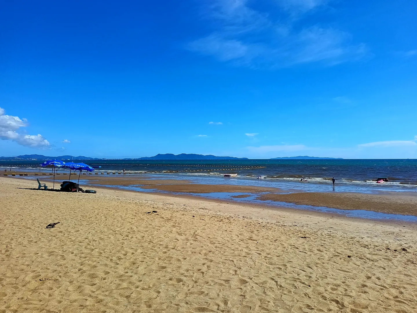 Sand and blue sea at Jomtien Beach, with umbrellas near the water.