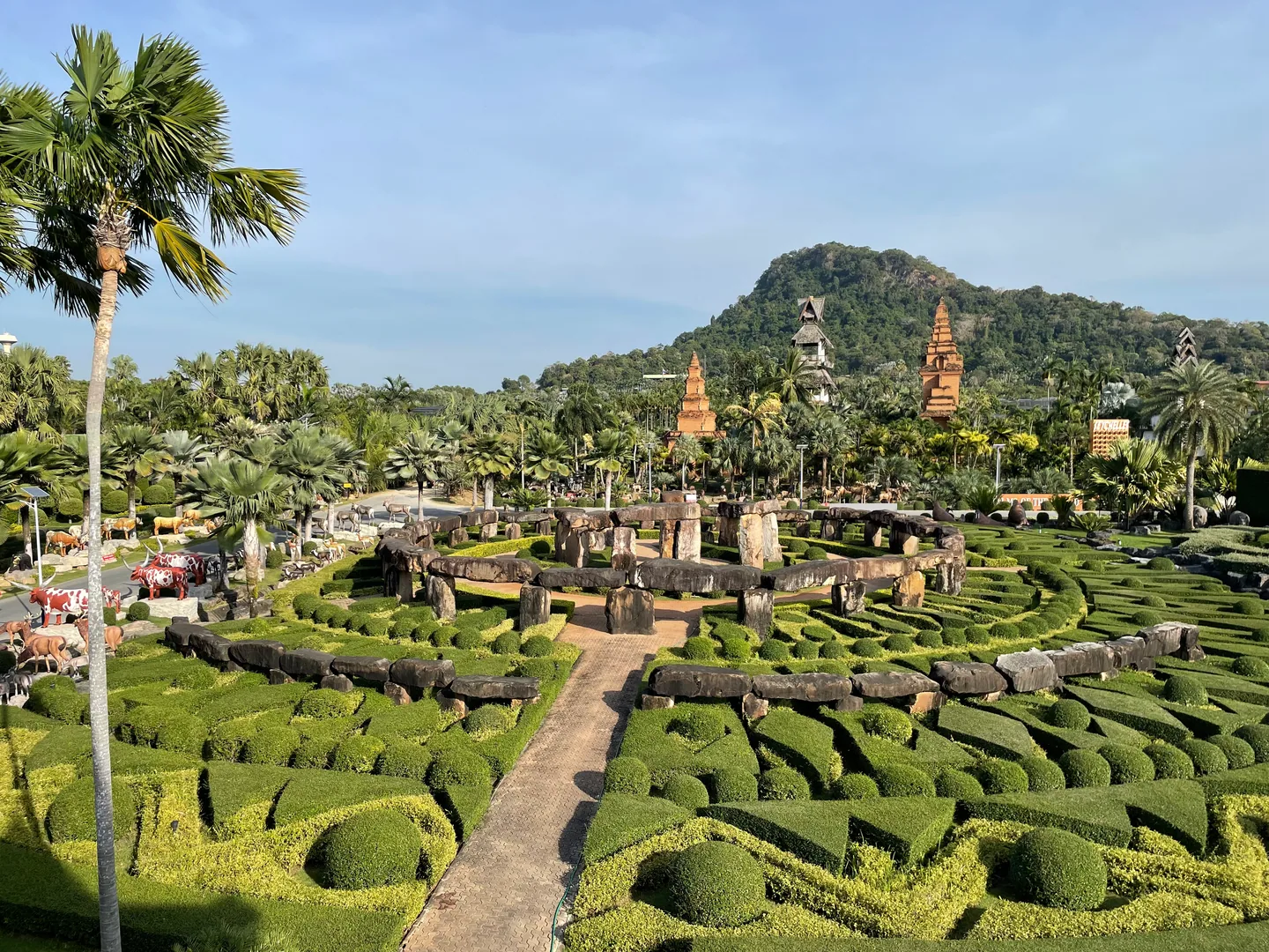 Geometric hedges and a stone-circle garden at Nong Nooch, with palms and hills behind.