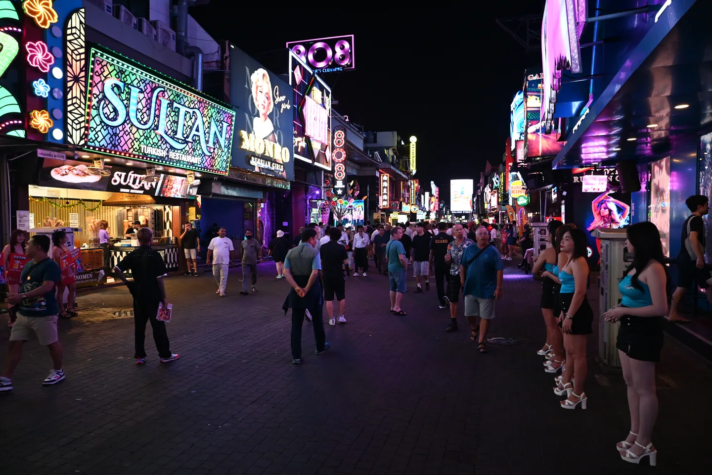 People walk along Walking Street between illuminated restaurant and nightlife signs.